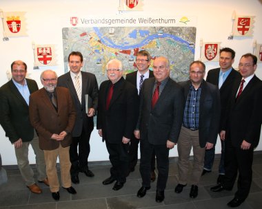 Vor einer Karte der Verbandsgemeinde Weißenthurm stehen die beteiligten Bürgermeister der angehörigen Kommunen und die zuständigen Verwaltungsmitarbeiter.